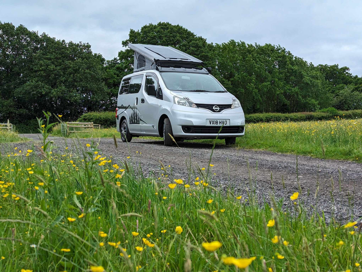 White micro campervan parked in a grassy field with pop-up roof open