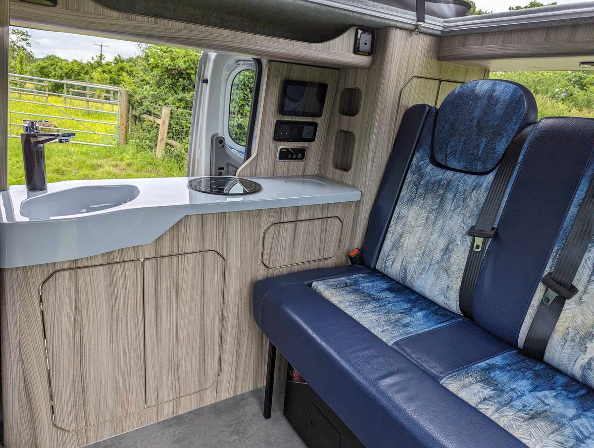 Camper van conversion bench with blue patterned seat and light wood cabinet paneling