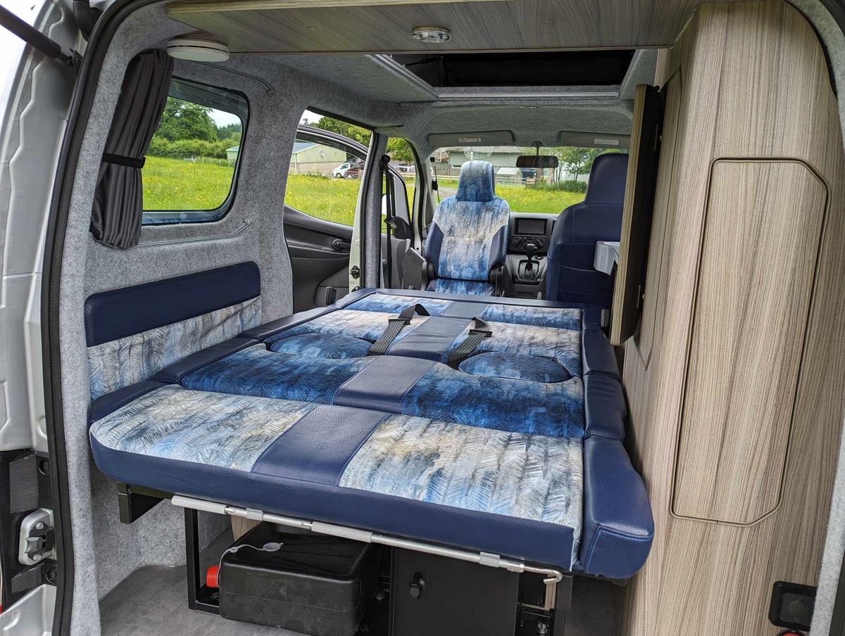 Camper van rear sofa with blue patterned cushions and fold-flat bed platform