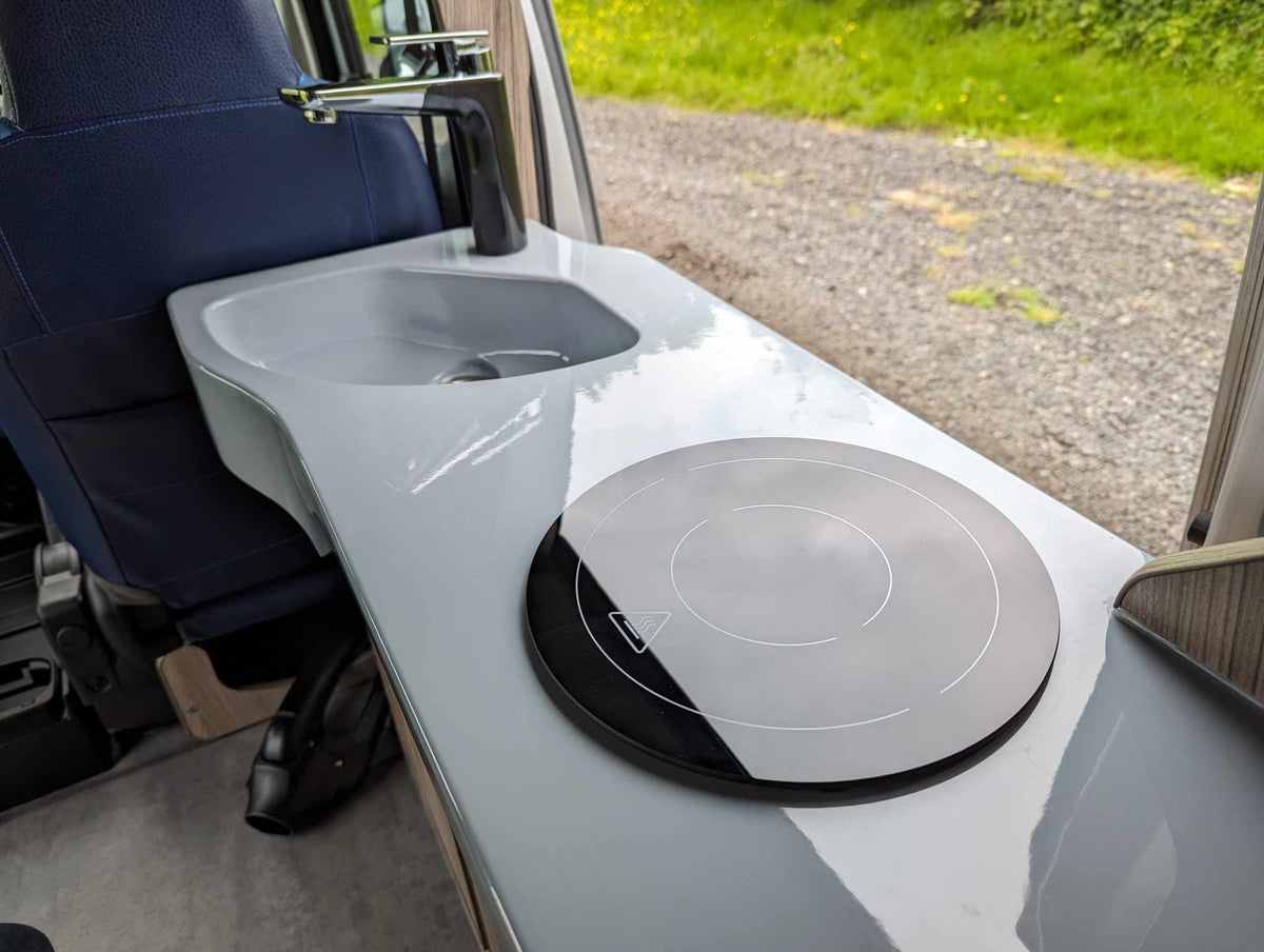 Camper van sink and hob unit with white countertop and circular cooktop