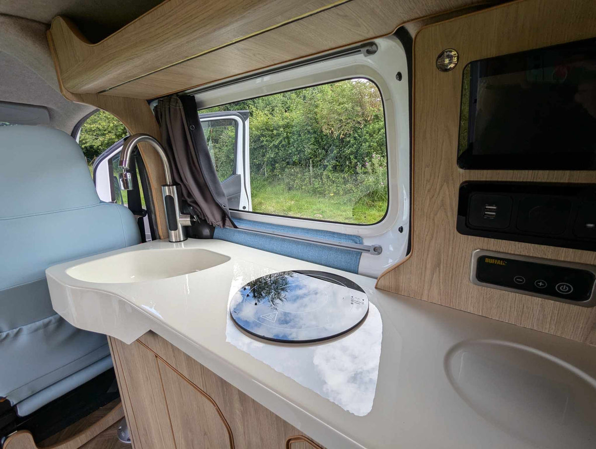 Micro campervan kitchenette with sink, countertop, and window under the ceiling storage