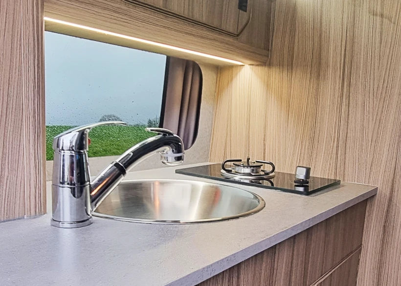 Campervan kitchen sink area with chrome faucet and stainless-steel worktop
