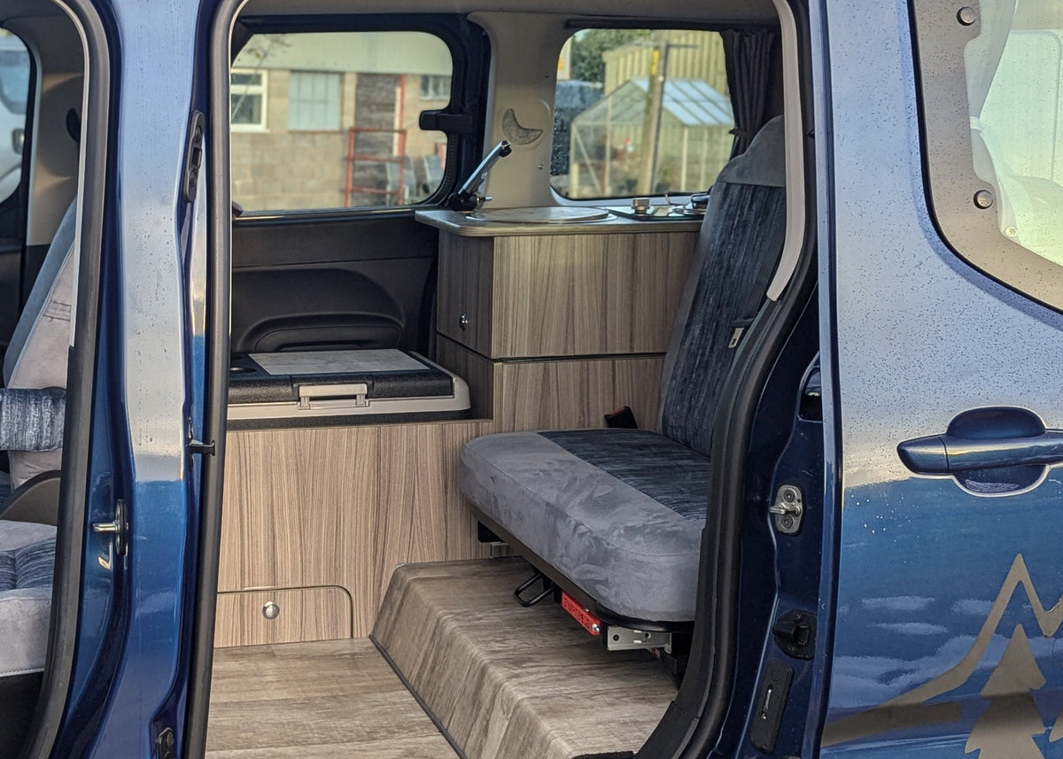 Camper van lounge area with wood galley cabinets and grey cushioned seating