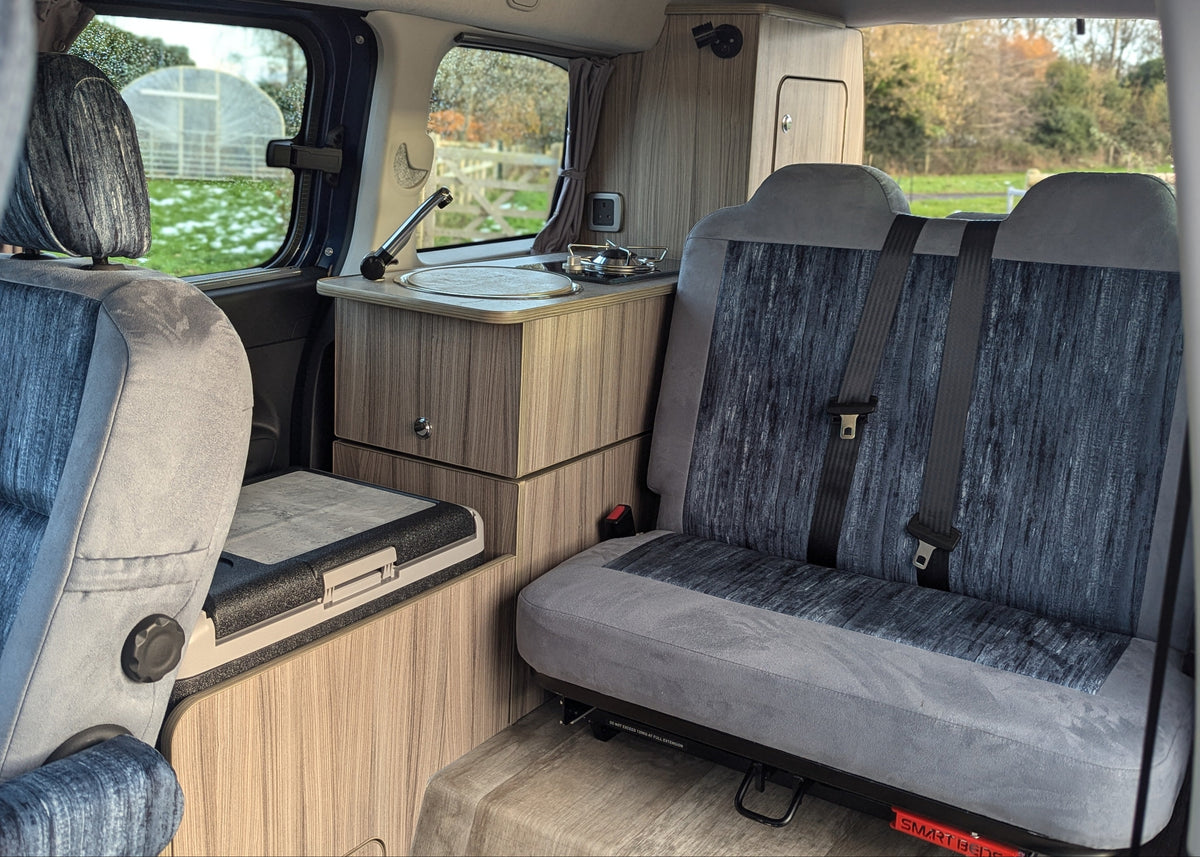 Campervan conversion galley cabinet, stove, and grey upholstery twin bench seating