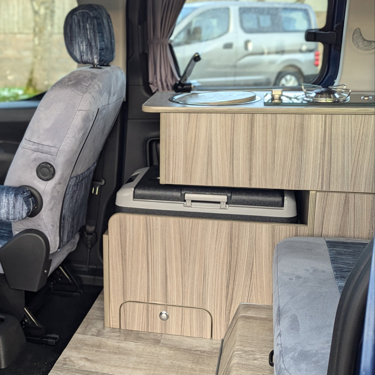 Light wood campervan kitchen unit with built-in sink and stovetop beside seats