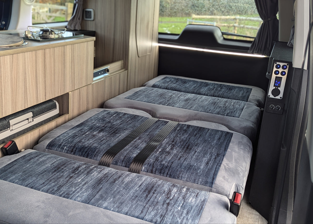 Campervan conversion interior with grey upholstered bed sections and control panel