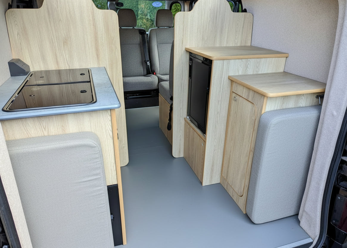 Campervan interior with bench seating, wood cabinetry, and rear kitchenette unit