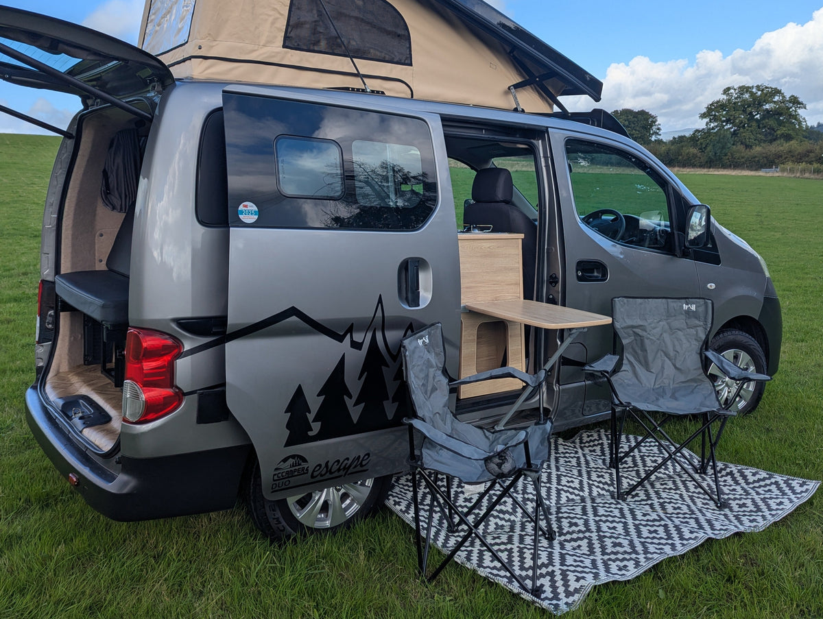 Micro campervan rear with bed platform, patterned rug, and side storage panel