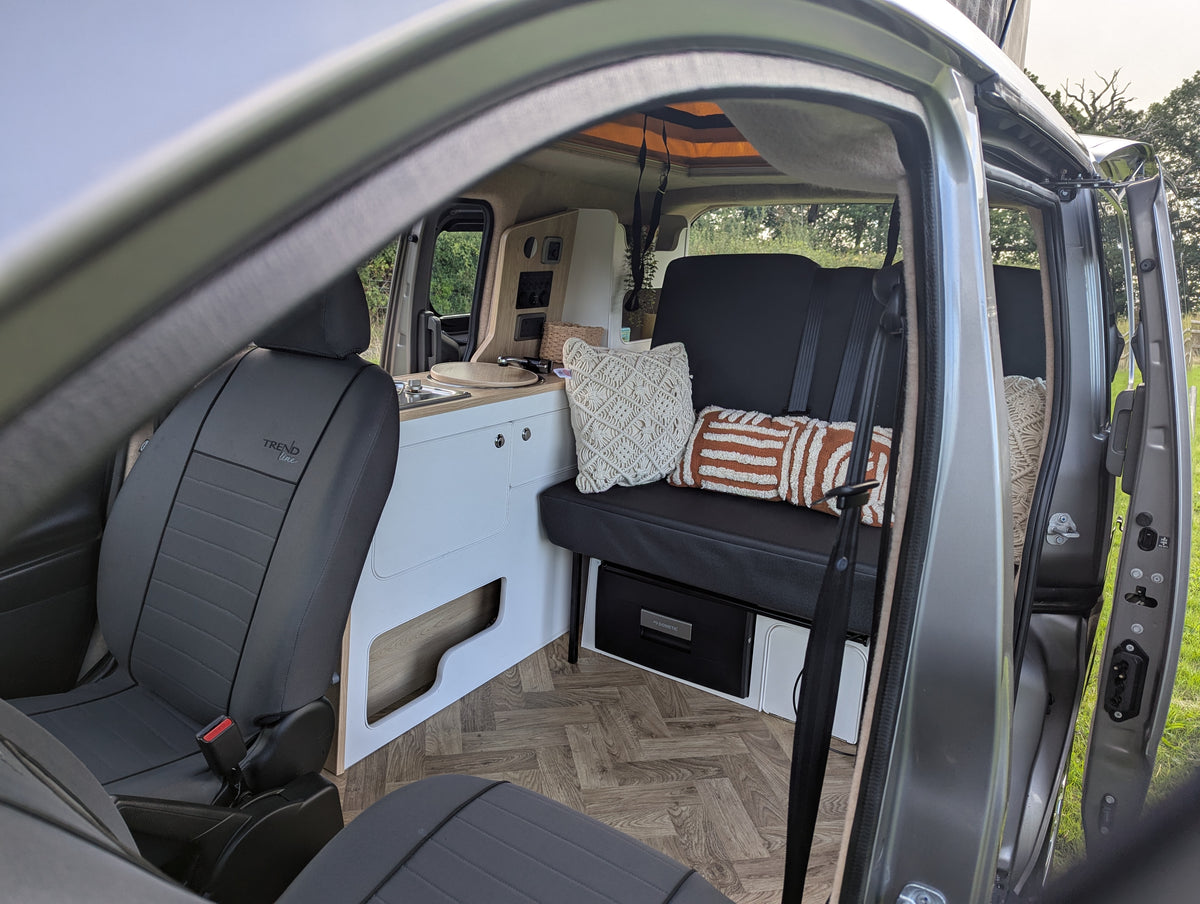 Micro campervan interior with two-tone bed base, seat bench, and patterned cushions