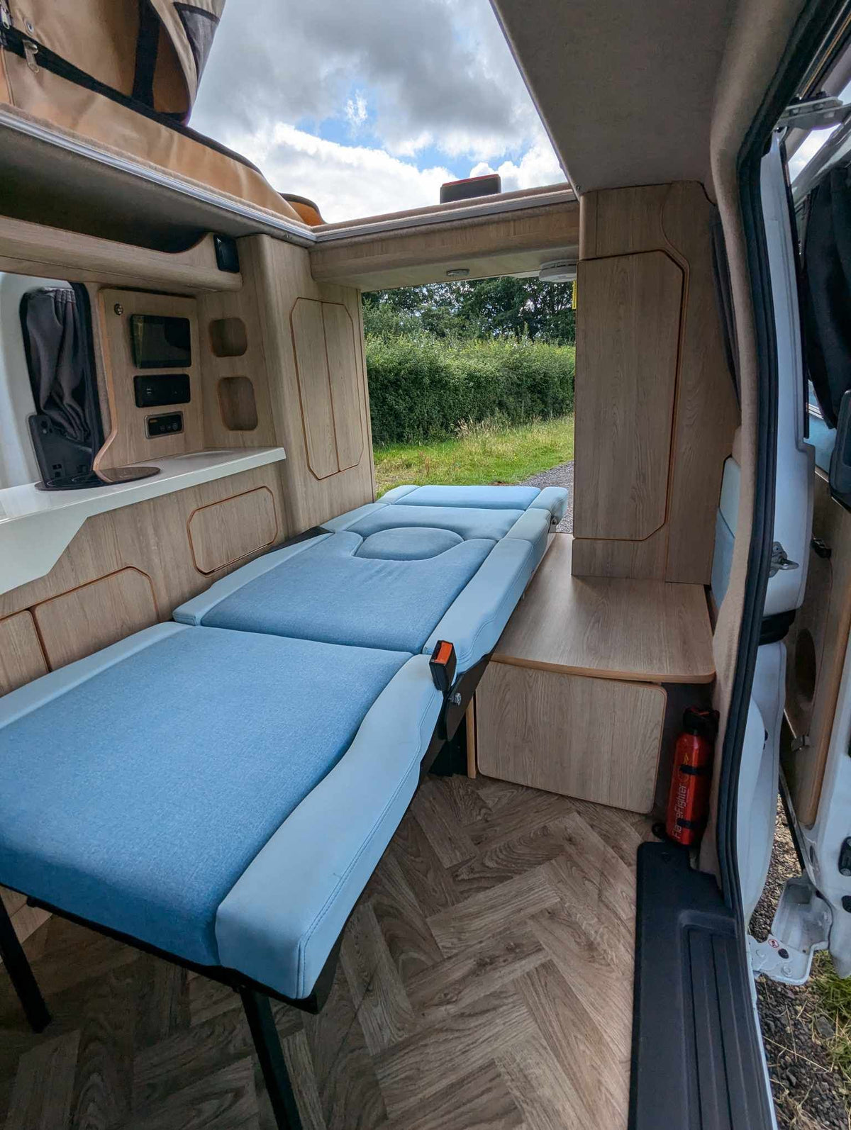 Solo travelling seat bed extended flat with blue cushions and light-wood cabinetry