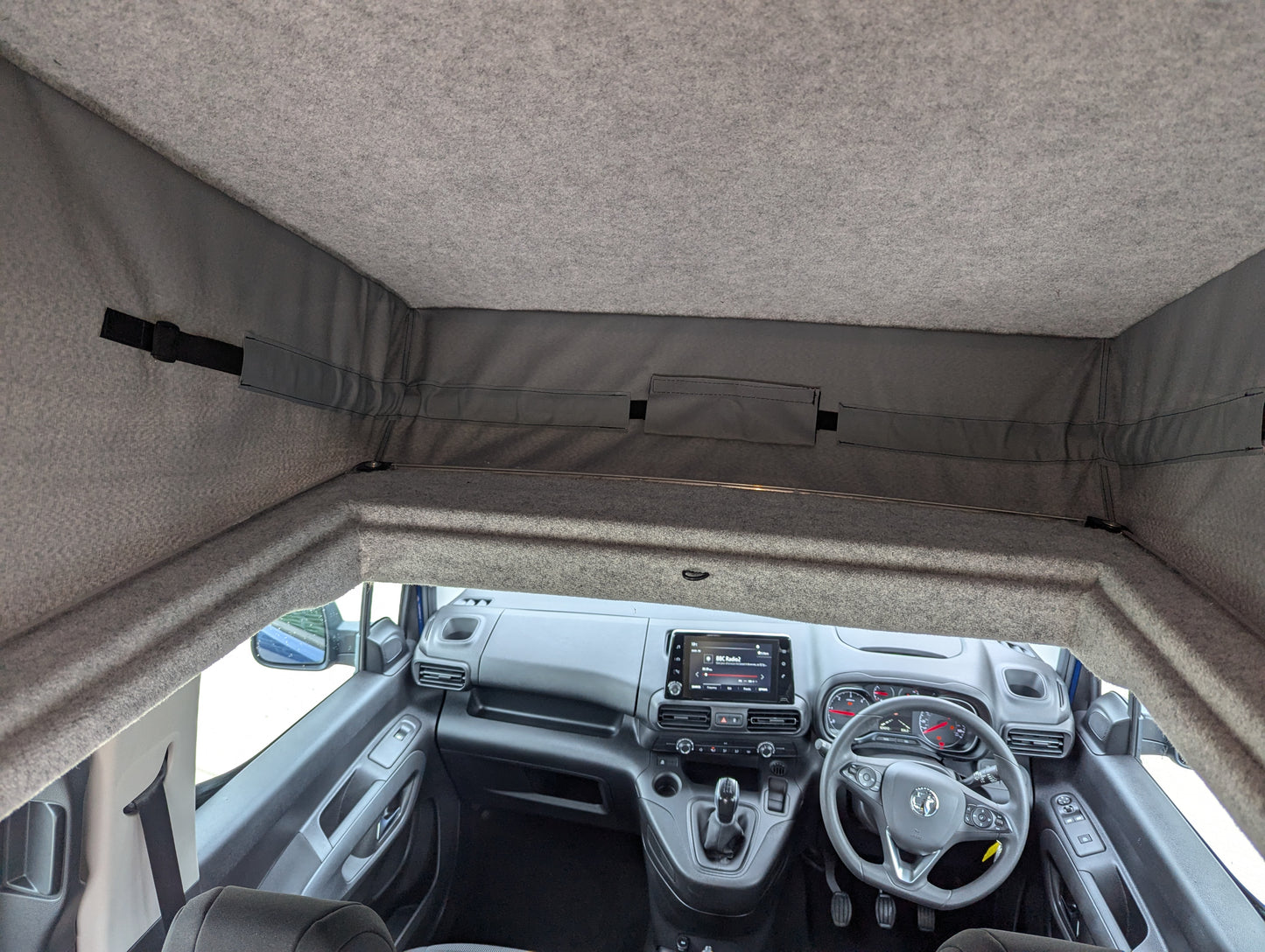Vehicle interior with pop-top roof raised; front seats and dashboard visible
