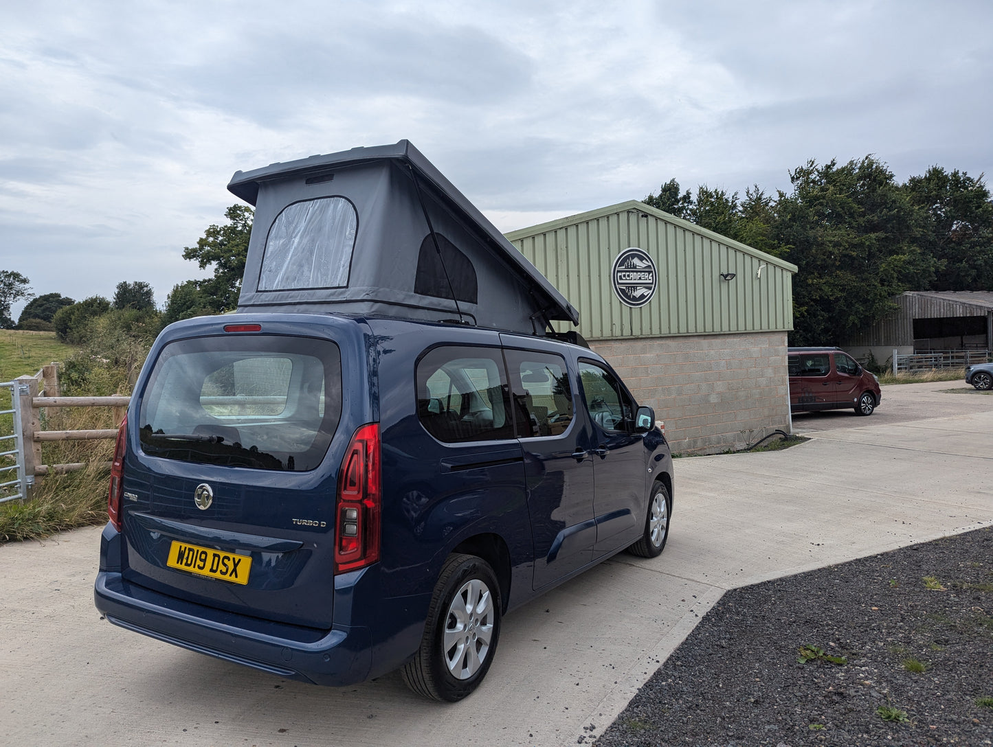 Dark blue van rear view with pop-top roof raised, canvas tent cover in place