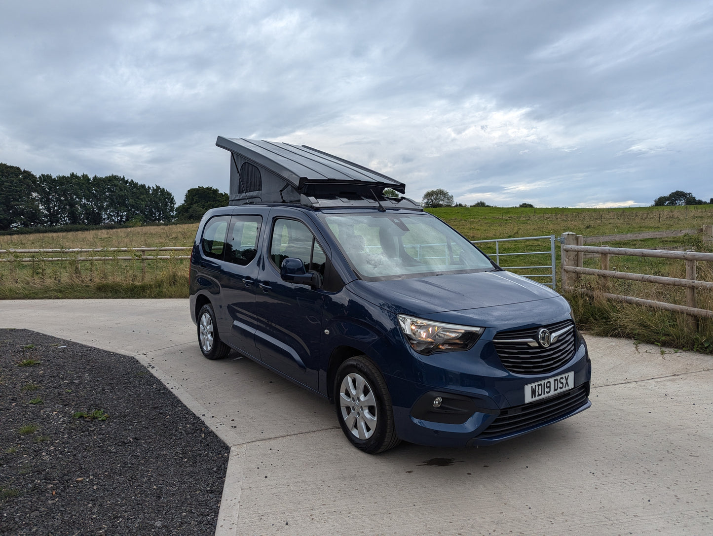 Dark blue van front three-quarter view with pop-top roof raised and canvas cover