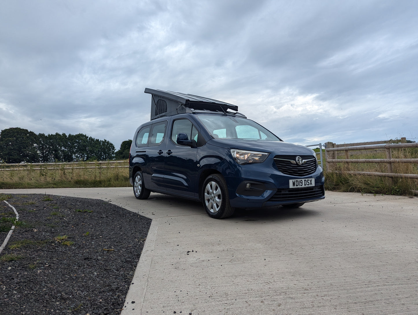 Dark blue van front view with pop-top roof raised, canvas tent cover visible