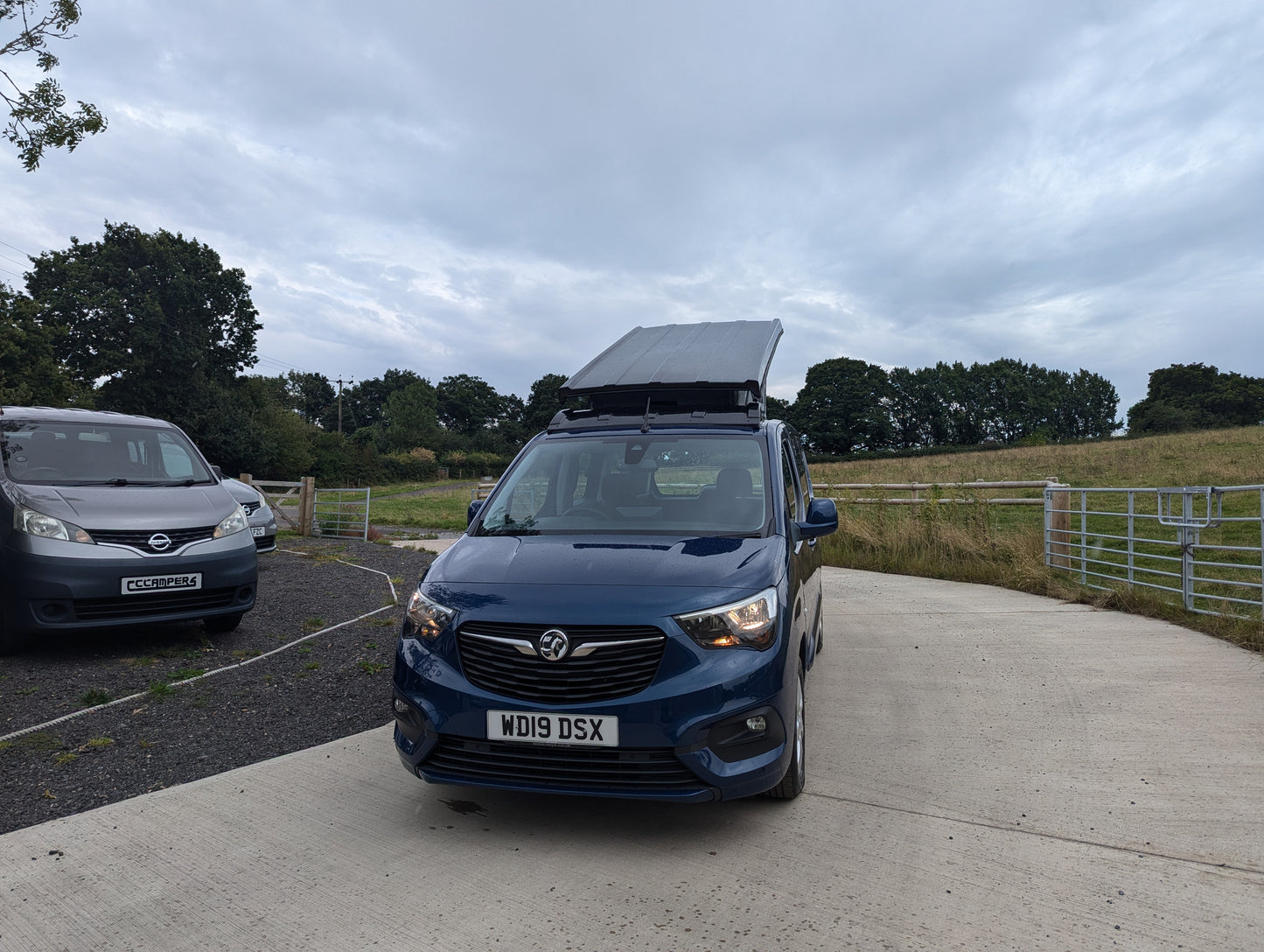 Dark blue van head-on view with pop-top roof raised, canvas tent cover