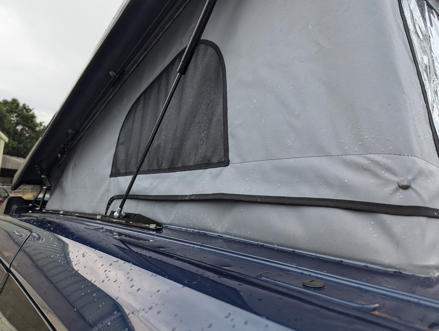 Dark blue van with pop-top roof raised, canvas tent cover over cabin