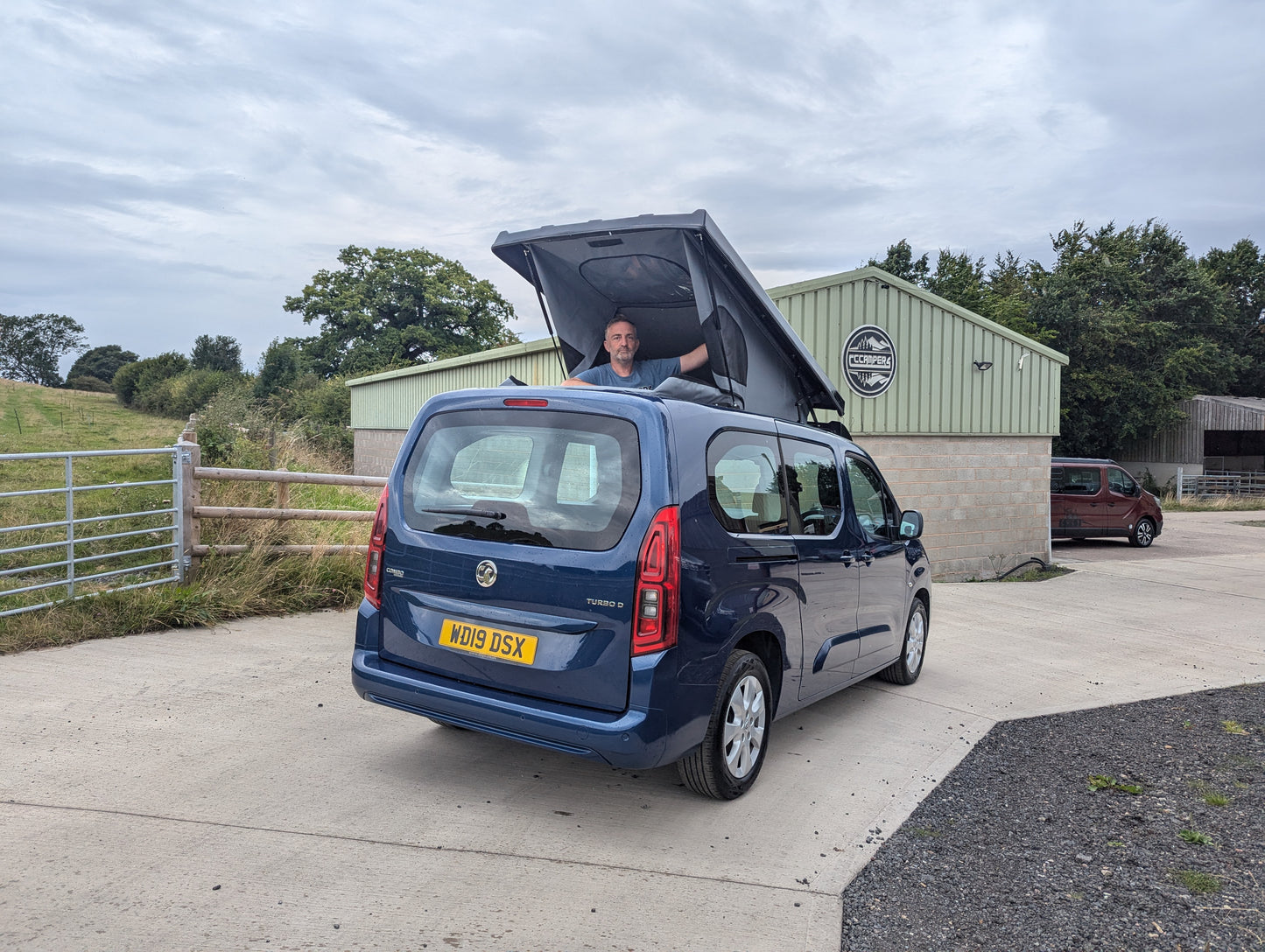 Dark blue van rear view with pop-top roof raised and canvas tent cover