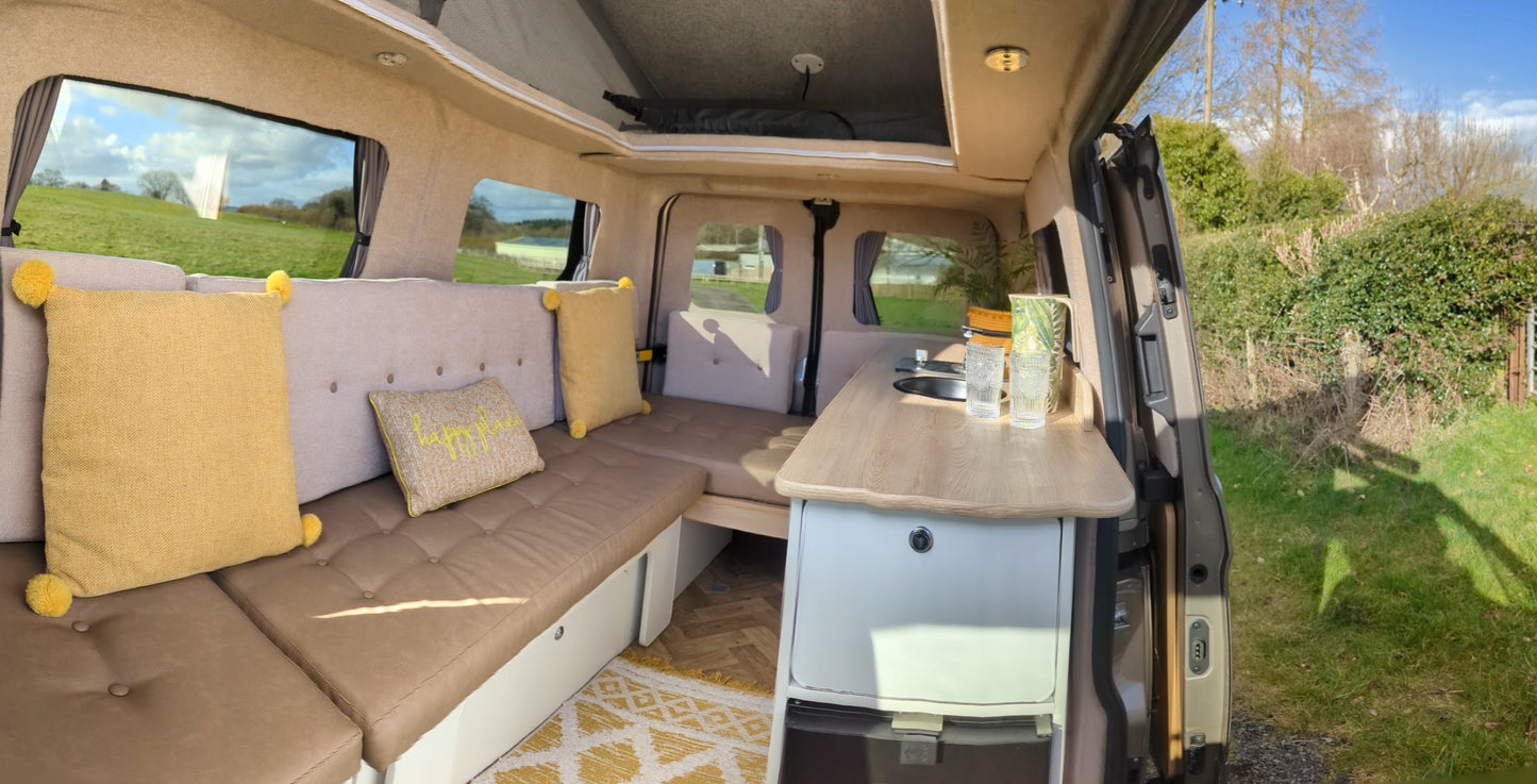 Camper van lounge with beige seating, window curtains, and side fold-out table