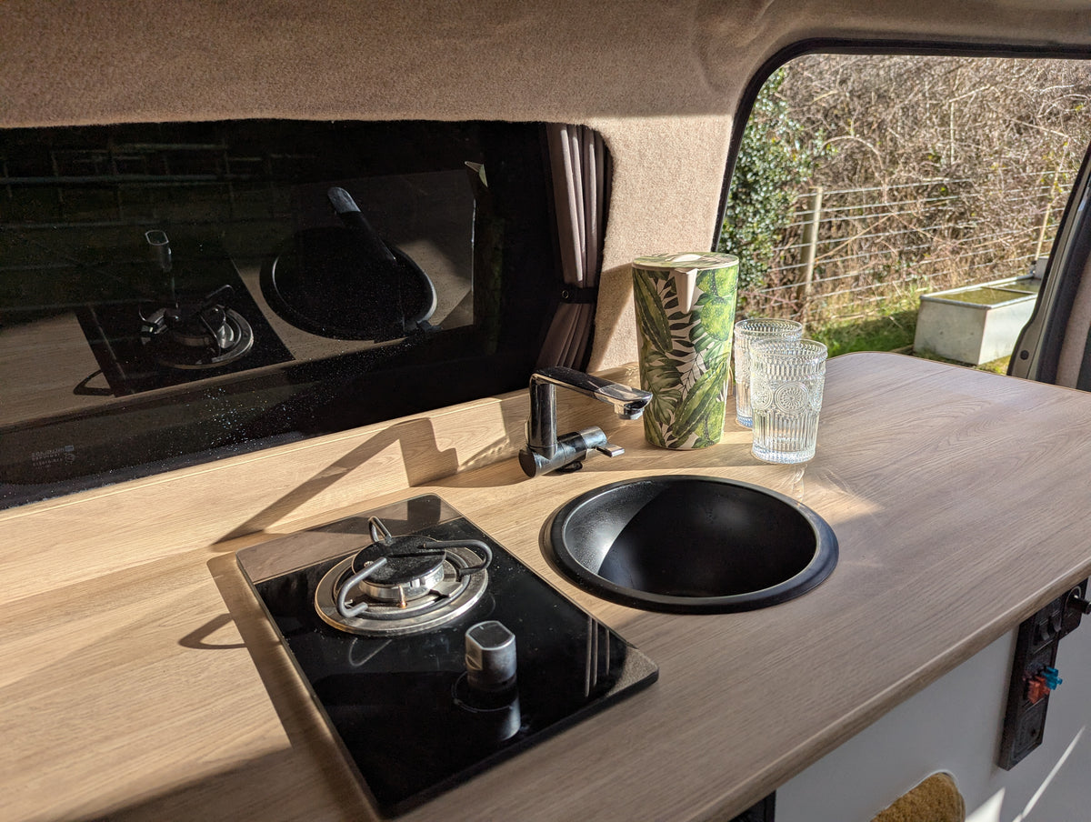 Camper van kitchenette with two-burner stove, round sink, and countertop