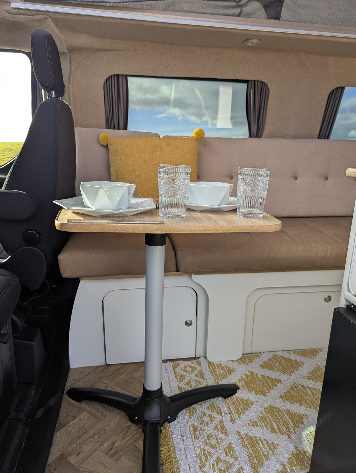 Camper van dinette with padded bench seating and table beside window curtains