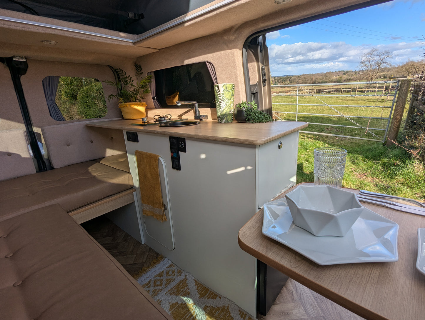 Camper van kitchen with white cabinets, countertop, and outdoor dining table