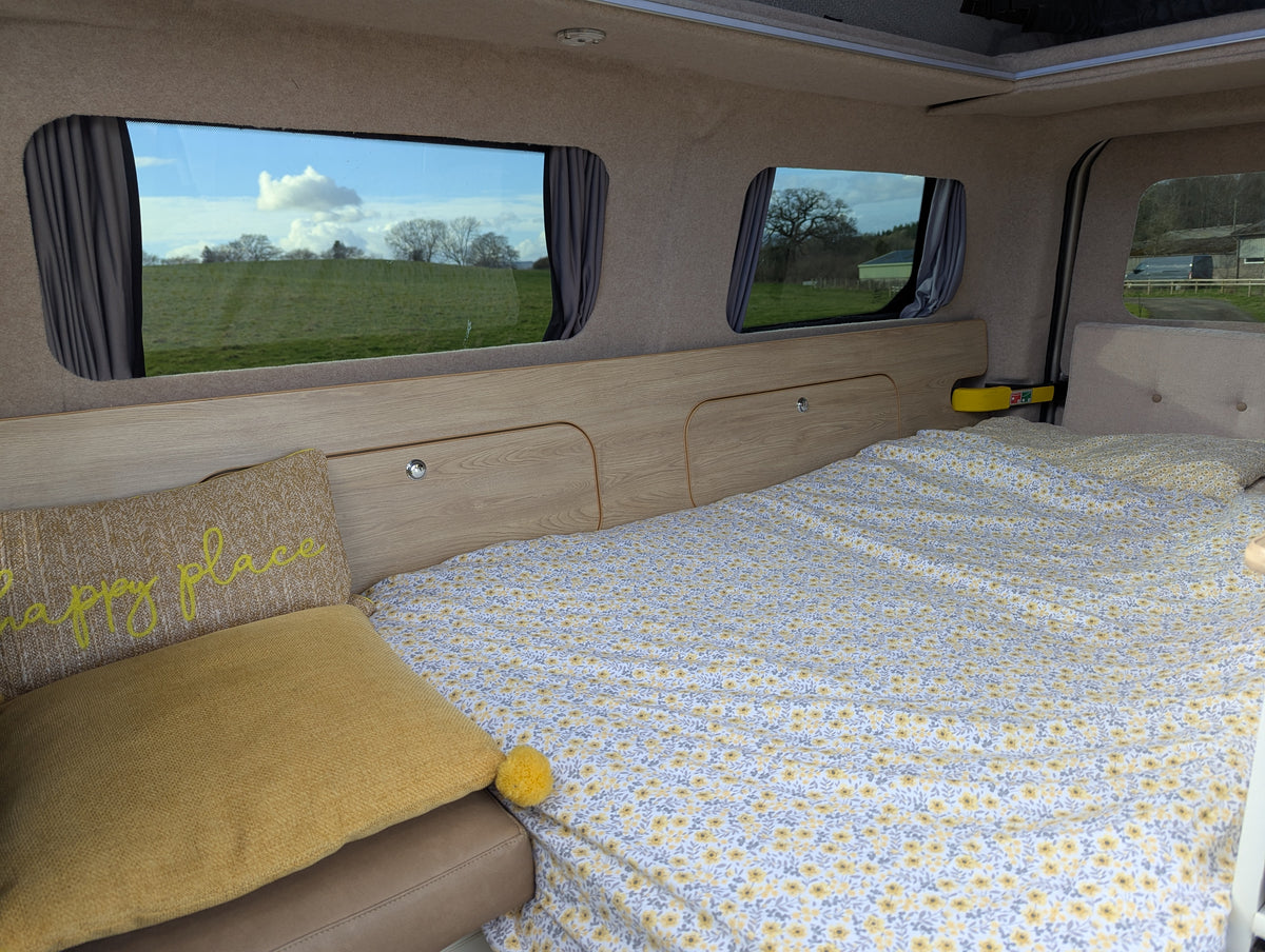 Camper van bed and seating corner with yellow cushions and patterned quilt