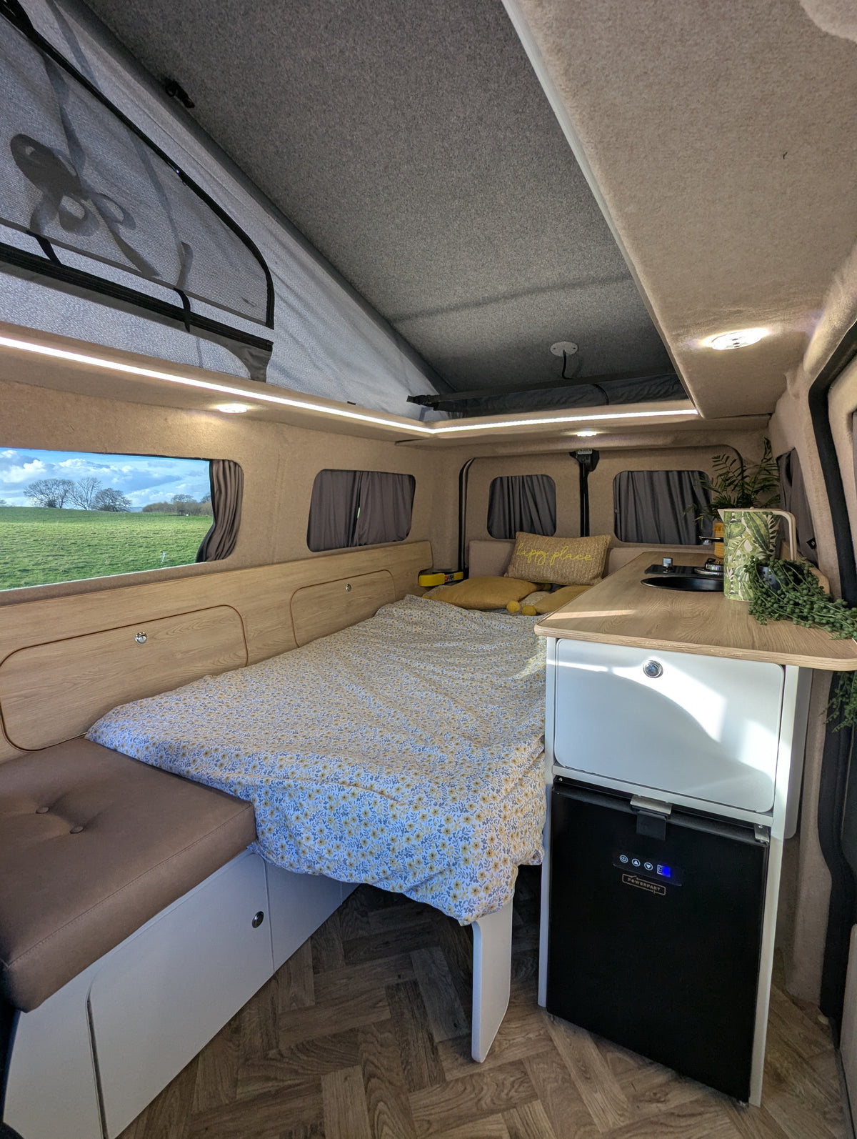 Camper van interior with bench seating, bed, kitchenette sink, and built-in fridge