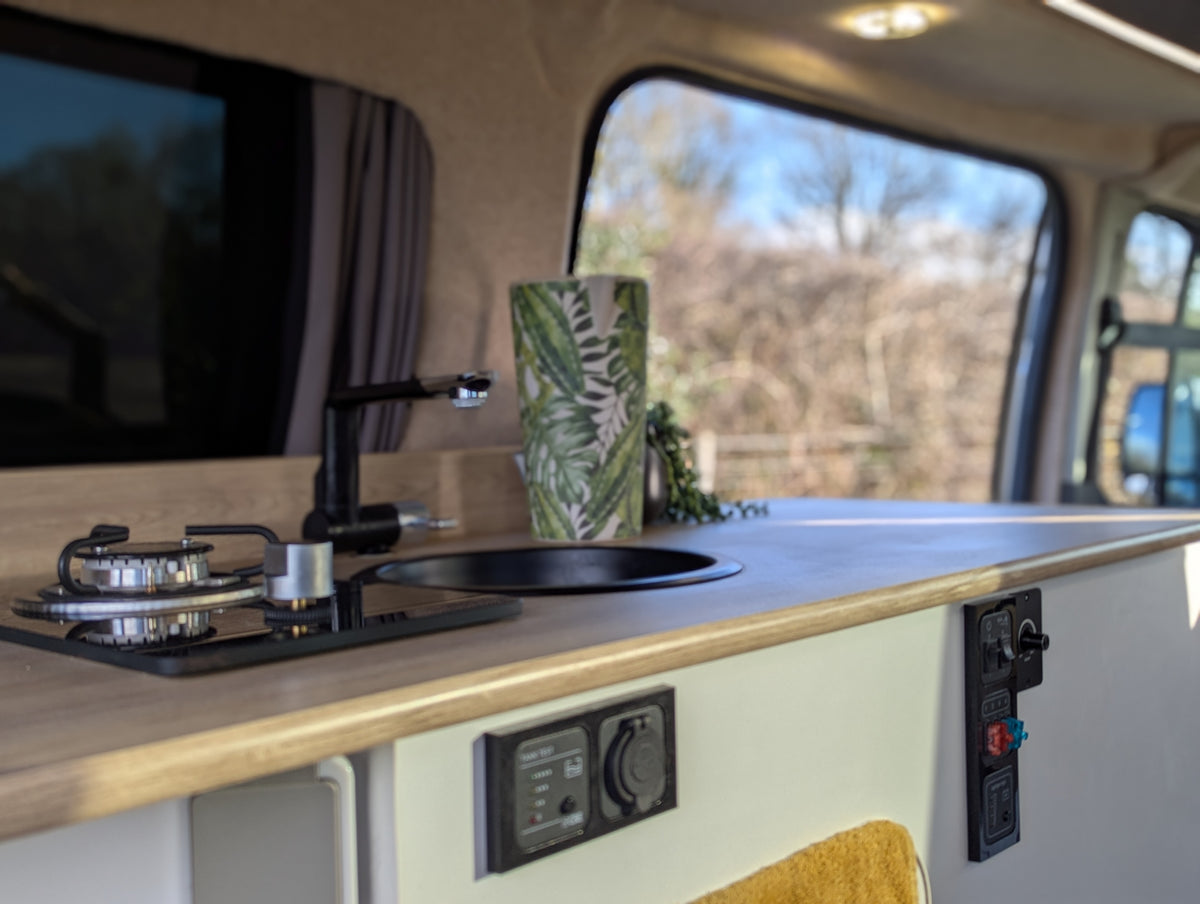 Camper van kitchenette with stovetop on wooden counter and electrical controls