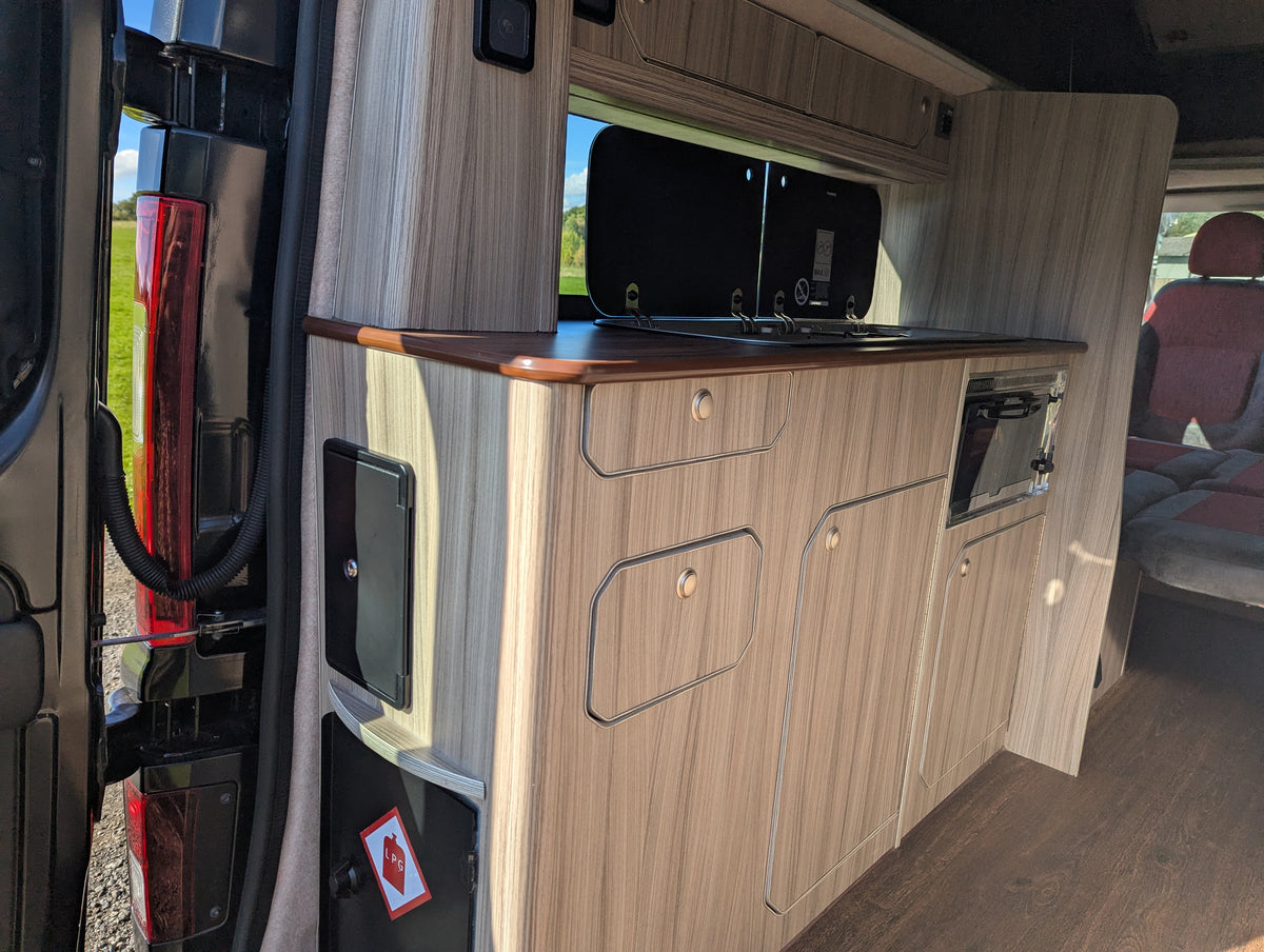 Campervan kitchen cabinet with light wood doors, drawers, and built-in countertop
