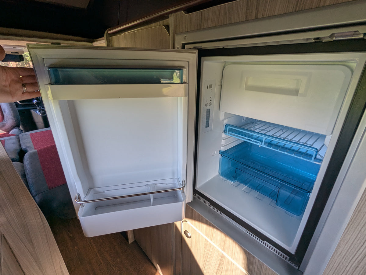Campervan fridge with open door and blue-tinted interior shelving
