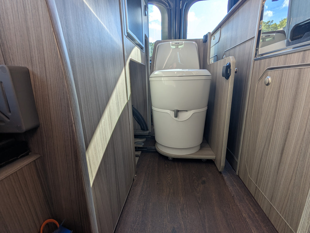 Campervan bathroom area with white toilet and wood-look wall panels