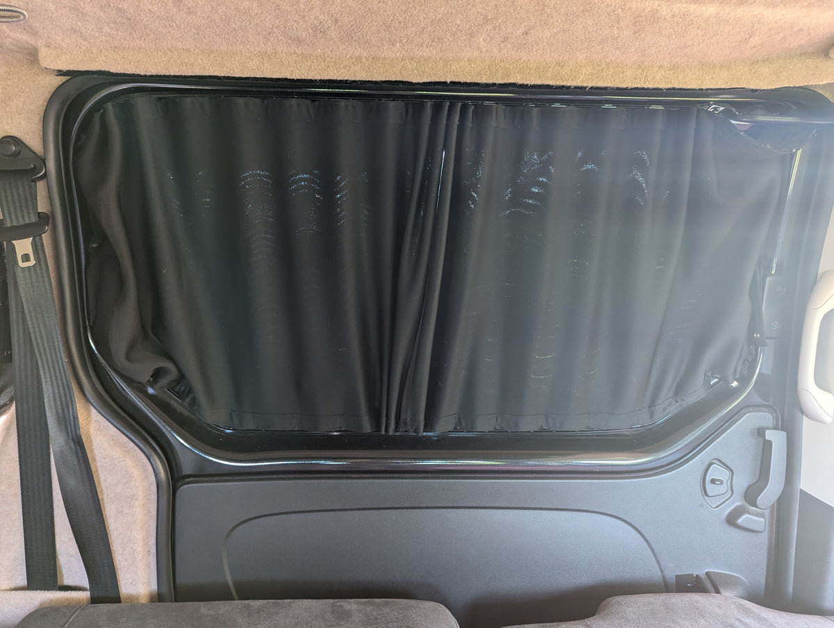 Campervan door window with black curtain and gray interior paneling visible