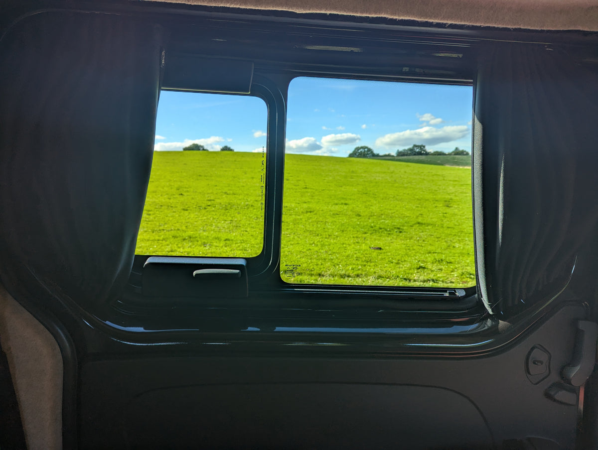 Campervan window opening showing green countryside view outside