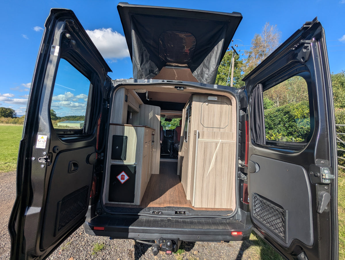 Open rear of campervan showing interior wood storage panels and doorway access