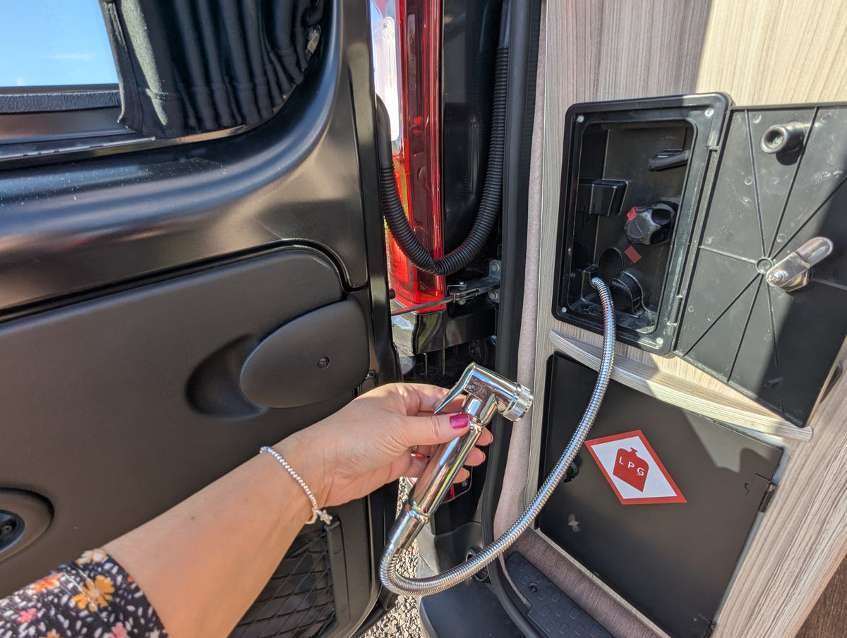 Campervan electrical hookup point with cables beside a service panel and warning sign