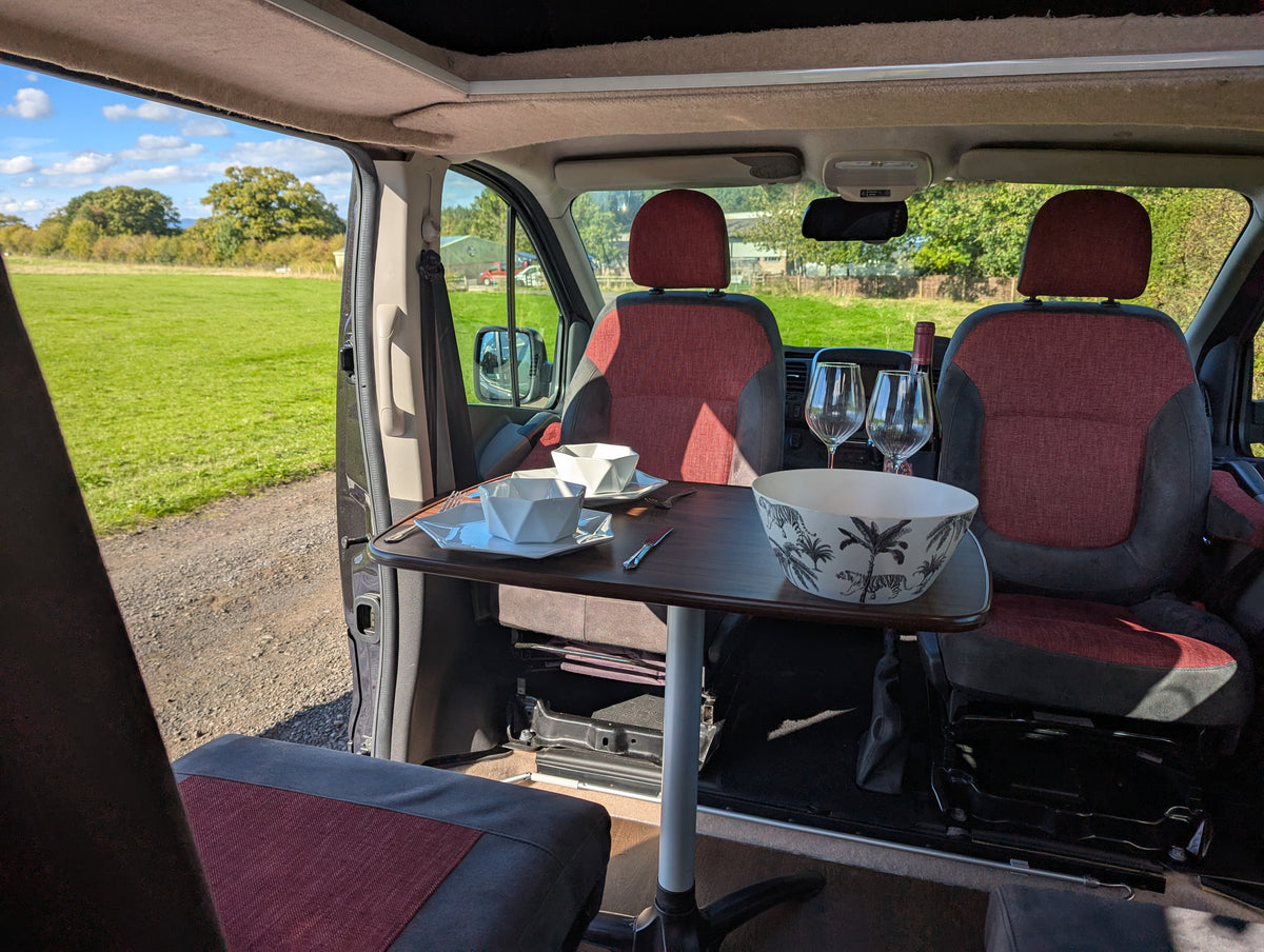 Campervan fold-out dining table with maroon seat cushions and two water carafes
