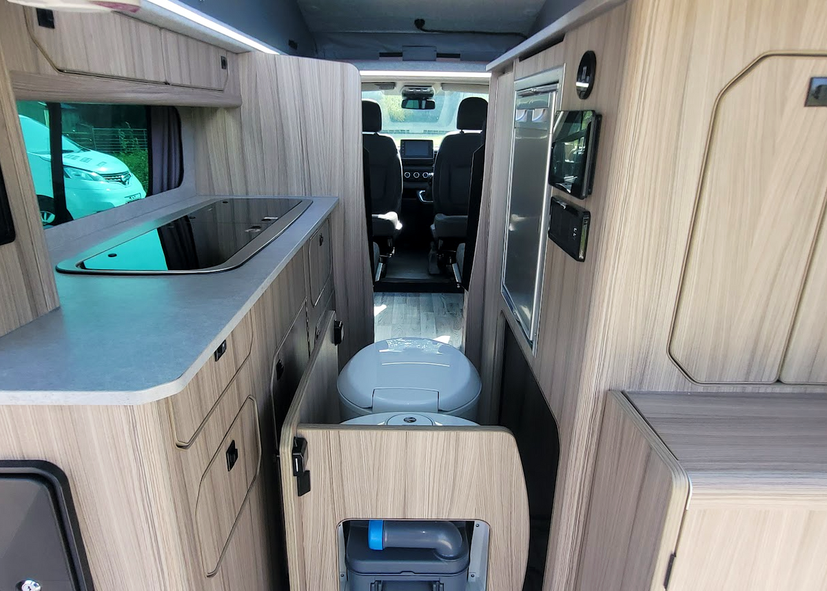 Campervan conversion interior with kitchen cabinetry, bench, and rear seating