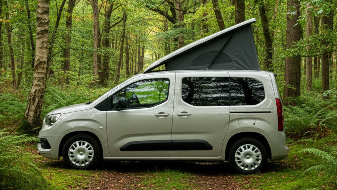 Camper van with pop-top roof elevated, black canvas tent on light gray body.