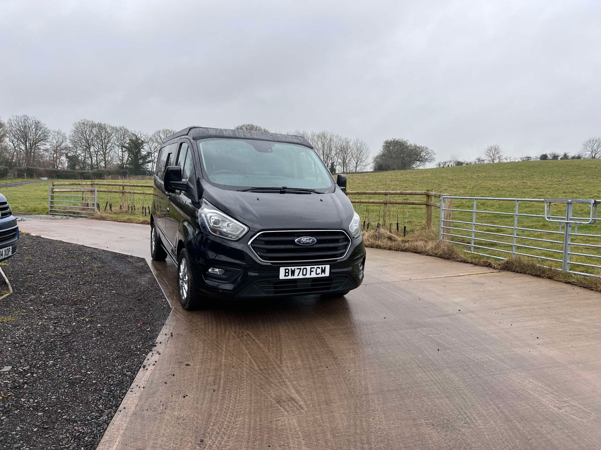 Black Ford van parked on a driveway with a rural landscape in the background