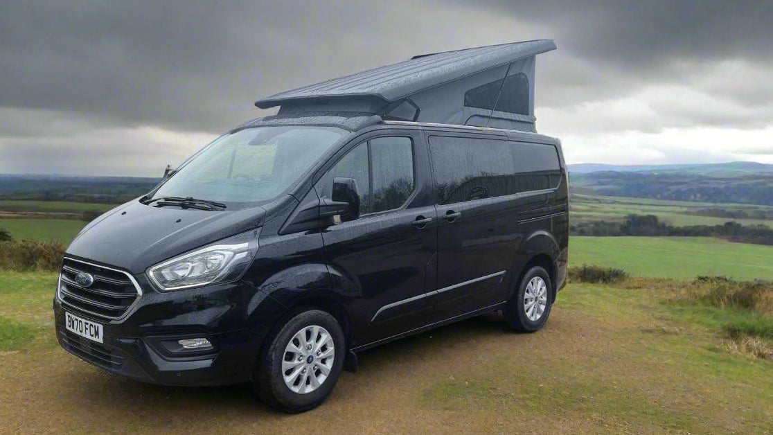 Black Ford Transit Custom pop-top roof van, three-quarter front view on rural road