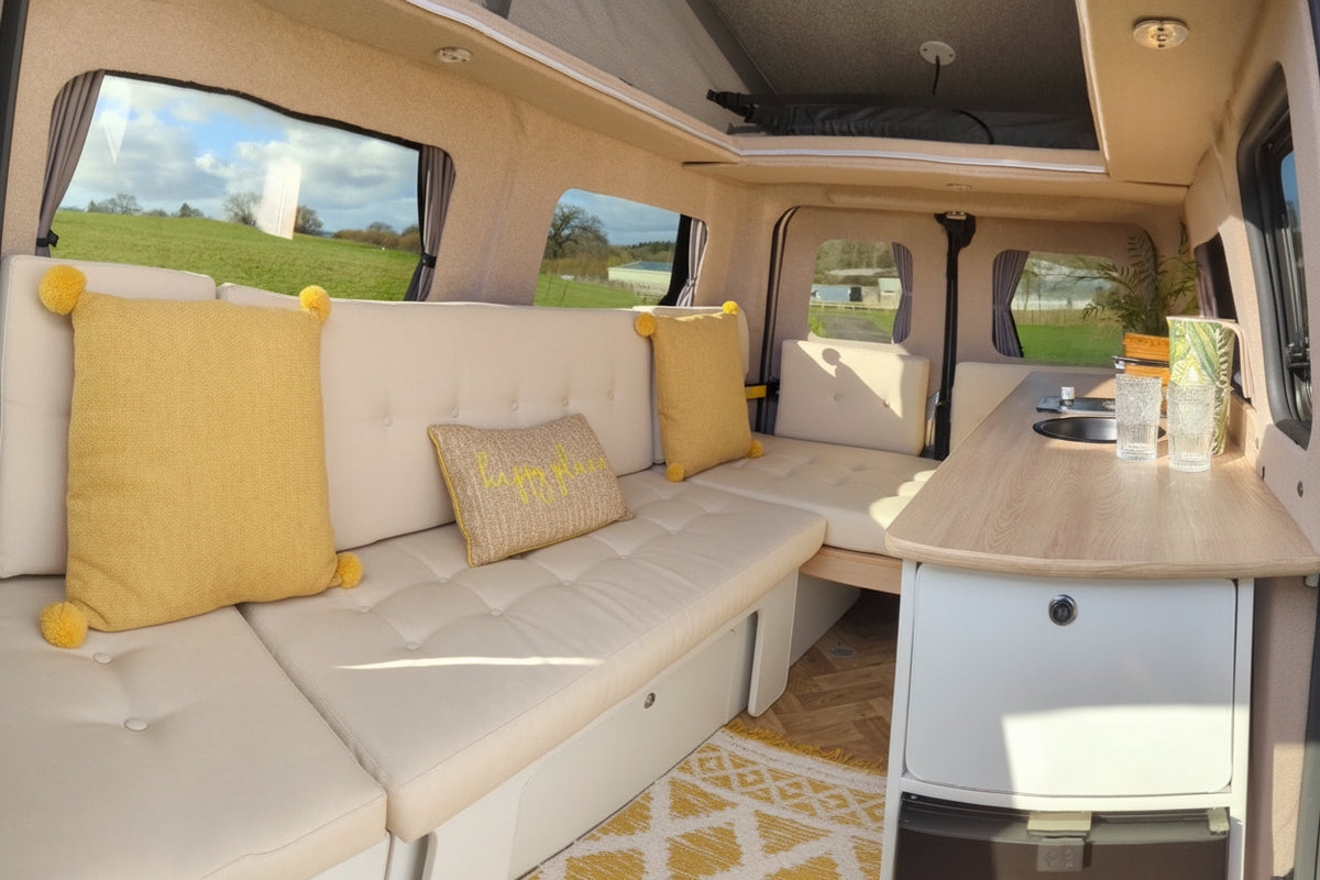 Campervan seating with yellow cushions, cabinet drawers, and side kitchenette counter