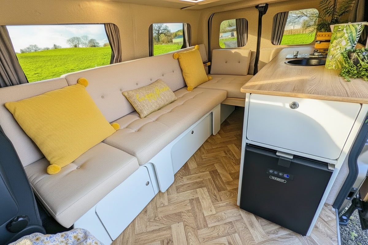 Campervan interior with L-shaped seating, storage cabinets, and built-in fridge