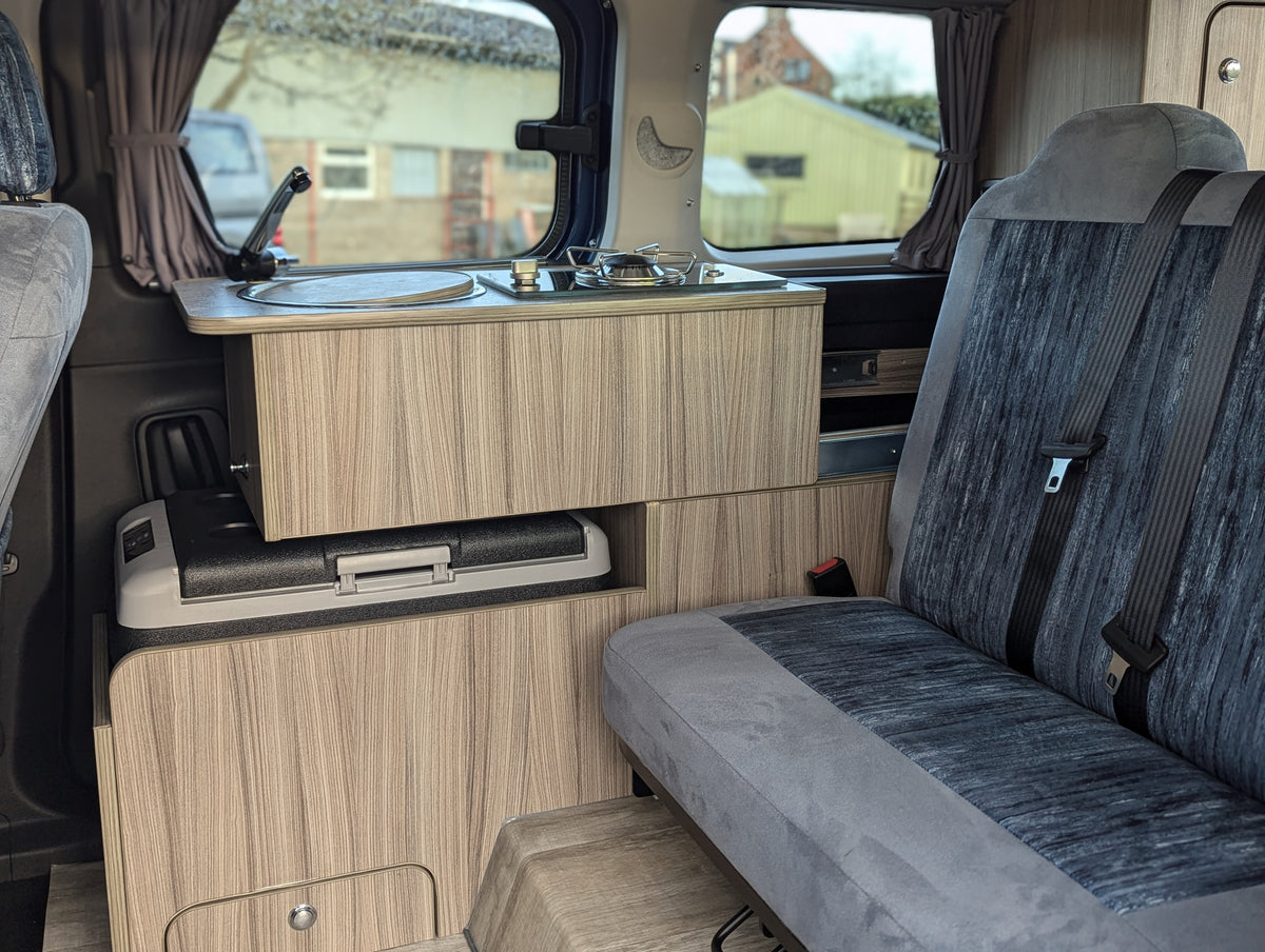Campervan lounge with wood cabinetry, countertop, stove setup, and grey bench seating
