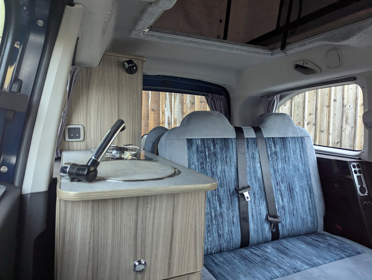 Campervan sleeping area with fold-out table and blue upholstered bed seats