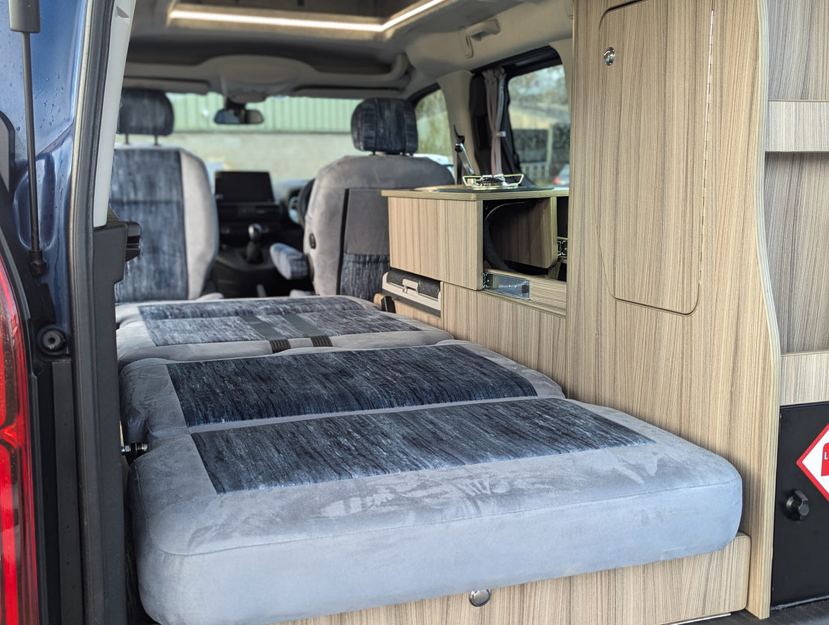 Campervan double bed with grey mattress, wood frame, and built-in side storage unit
