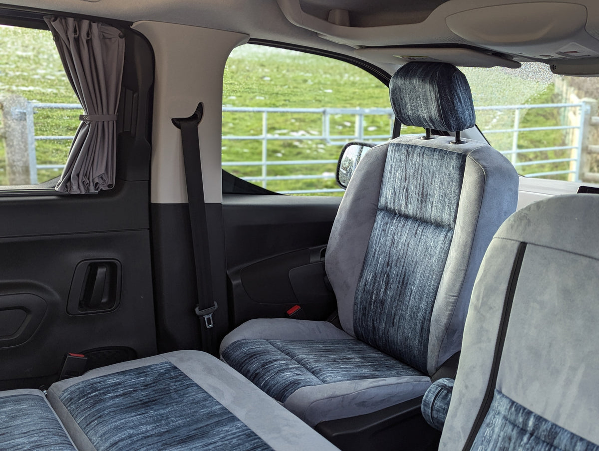 Campervan rear bench seat setup with grey upholstery and seatbelts near side windows