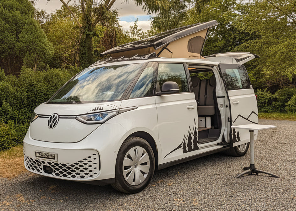 A white Volkswagen vw id buzz camper van parked on a gravel surface outdoors, with trees, bushes, and a blue sky with clouds in the background. The side door and pop-up roof are open.