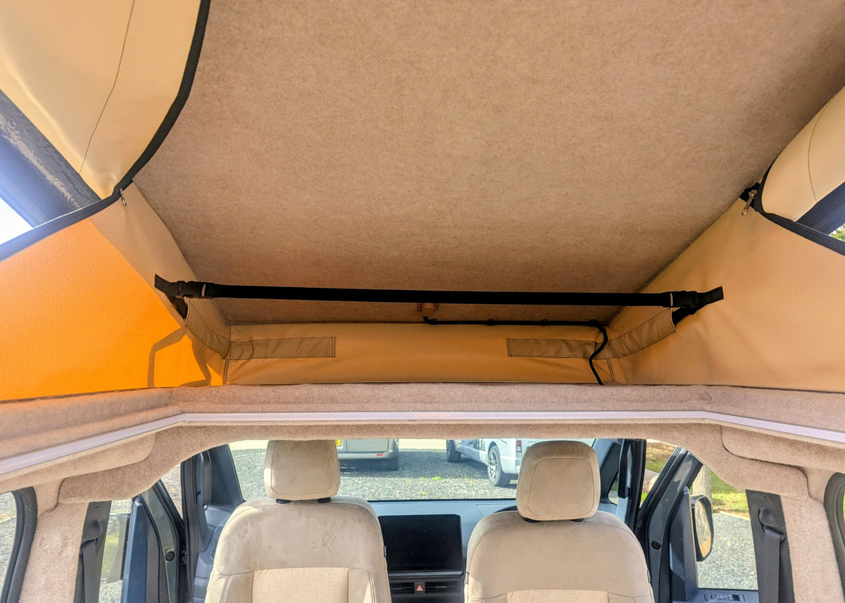 Interior perspective looking upwards into the elevated pop-top roof structure showing the beige fabric tent lining and integrated ceiling support framing. over head storage