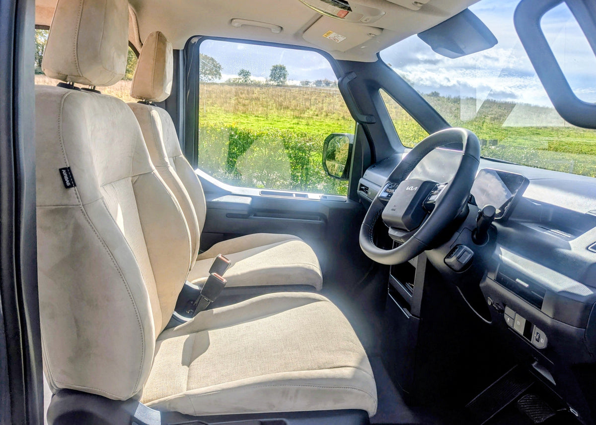 Front cabin view showing the steering wheel, digital instrument cluster, and passenger seats overlooking a rural landscape in the Kia PV5 Witley.