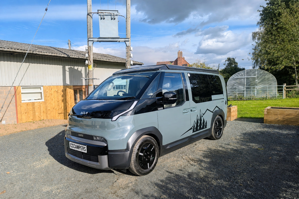 Clean front three-quarter exterior view of the grey Kia PV5 Witley electric campervan parked outdoors in daylight, highlighting its futuristic front styling.
